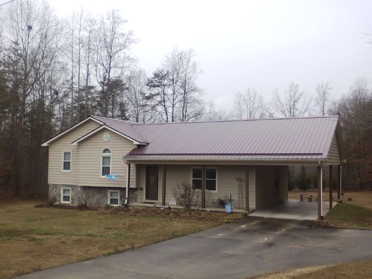 Burgundy metal roof on a tan split level home with an attached carport in Colton
