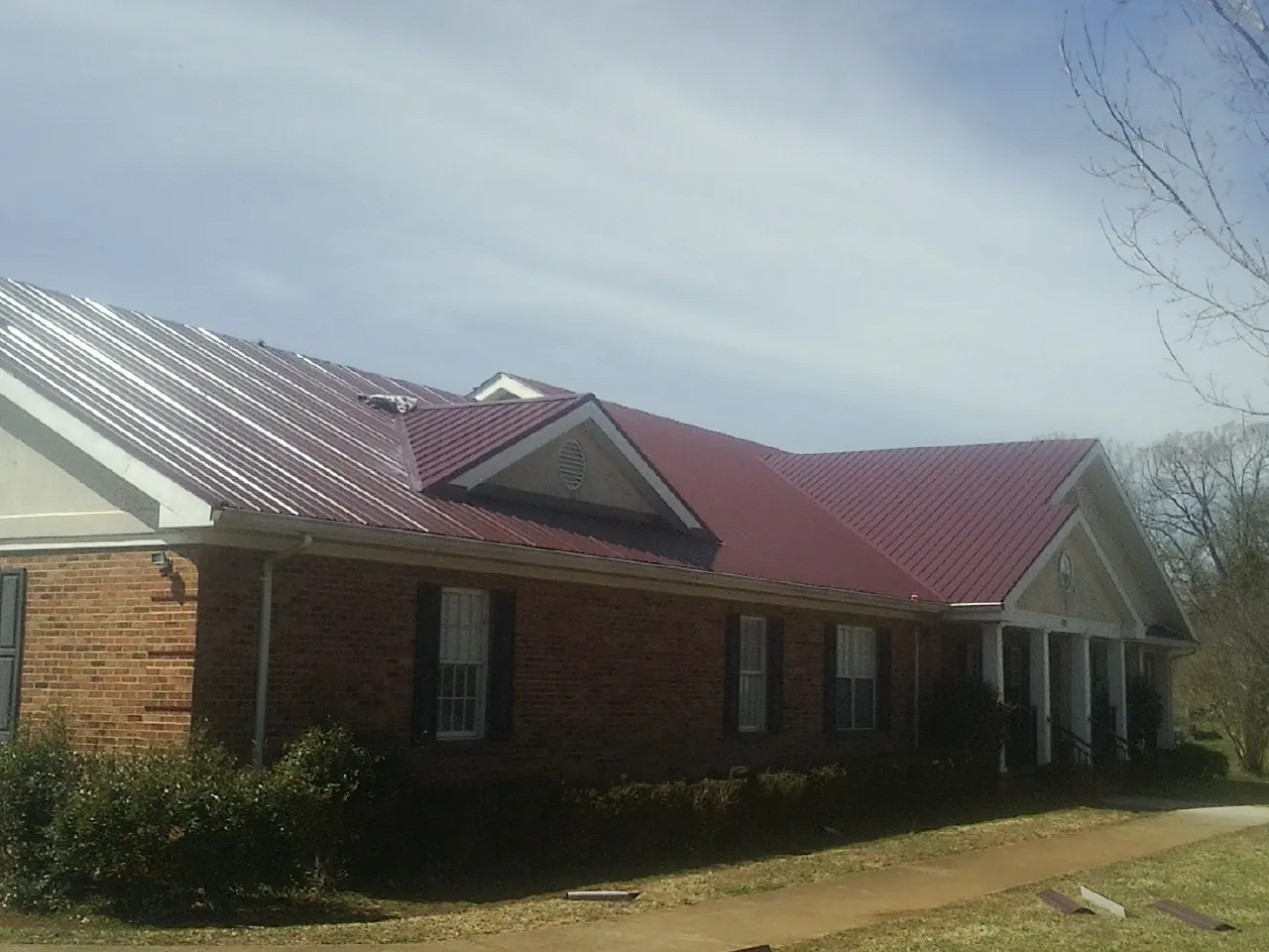 Red metal roof with gabled entries on a long brick building, from a Hail Damage Roof Repair job in Colton