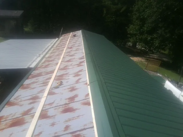 Old rusted panels beside newly installed green metal roofing — Wind Damage Roof Repair by Roofing Brothers in Colton