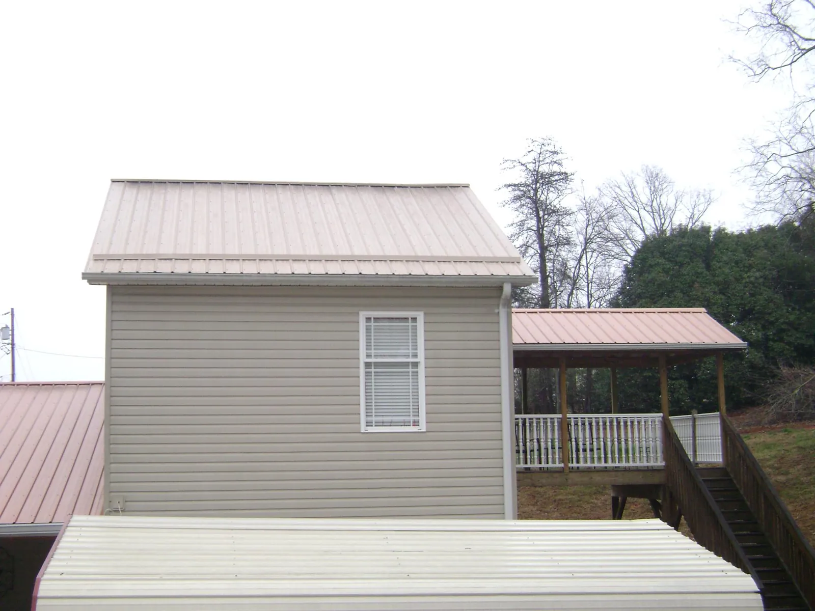 Tan metal roofs on a two story addition and attached porch, from a Roof Replacement job in Colton